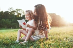 Learning is fun. Mother and daughter sitting and reading the little book with heart on it's cover