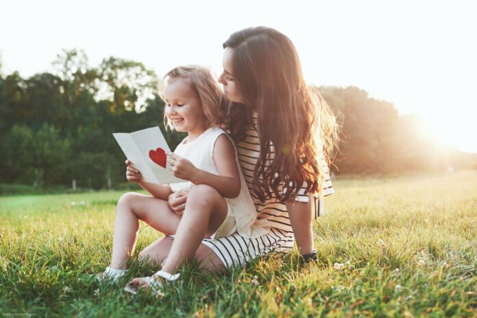 Learning is fun. Mother and daughter sitting and reading the little book with heart on it's cover Learning is fun. Mother and daughter sitting and reading the little book with heart on it's cover