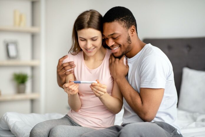 Portrait of joyful interracial couple looking at positive pregnancy test indoors Portrait of joyful interracial couple looking at positive pregnancy test indoors