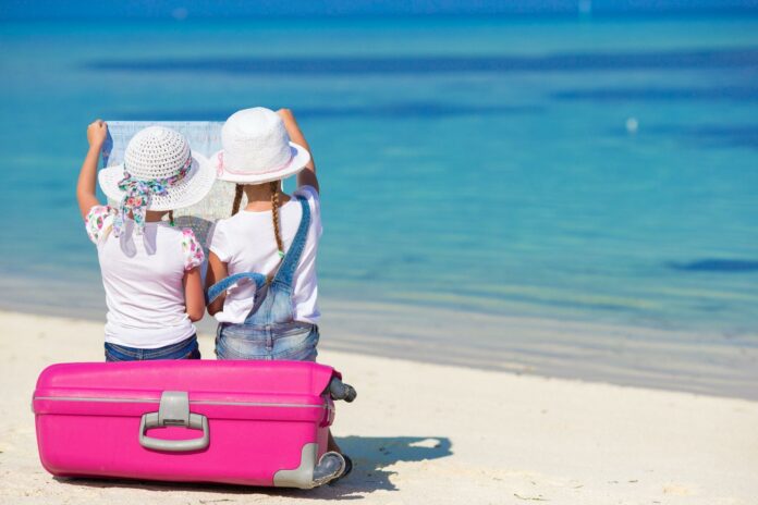 Little girls with big suitcase and map at tropical beach Little girls with big suitcase and map at tropical beach