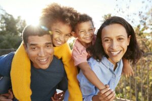 Young mixed race parents parents having fun piggybacking their children in the garden