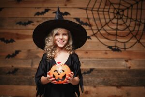 Halloween Witch concept - little caucasian witch child enjoy with halloween candy pumpkin jar. over