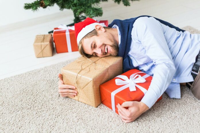 Christmas and holidays concept - Happy man in santa hat opening a gift at home in the living room