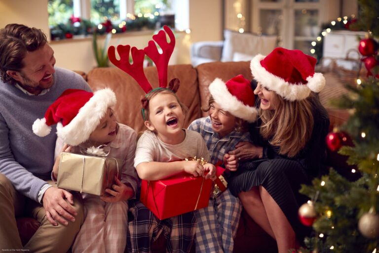 Family Wearing Santa Hats Sitting On Sofa At Home Opening Christmas Gifts